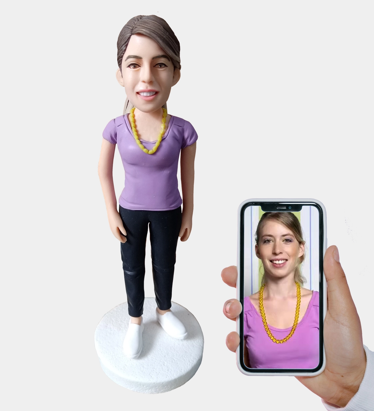 Custom clay figurine made from a woman's photo displayed on a smartphone. Personalized handcrafted sculpture gift.